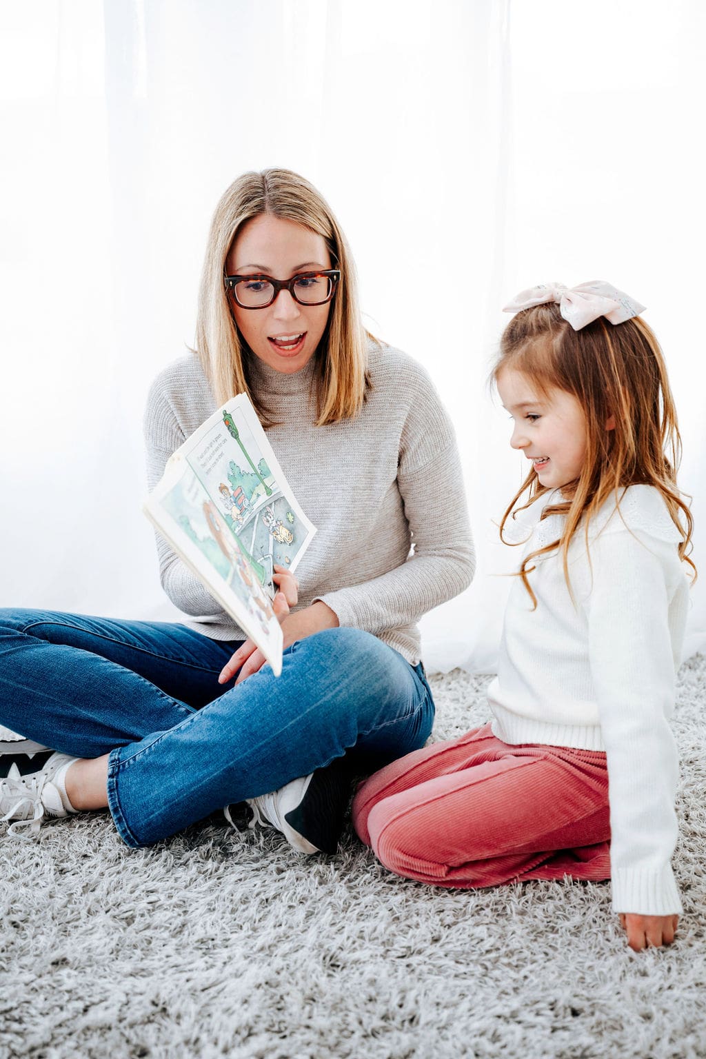 Speech therapist reading a book to a smiling young girl during a pediatric therapy session